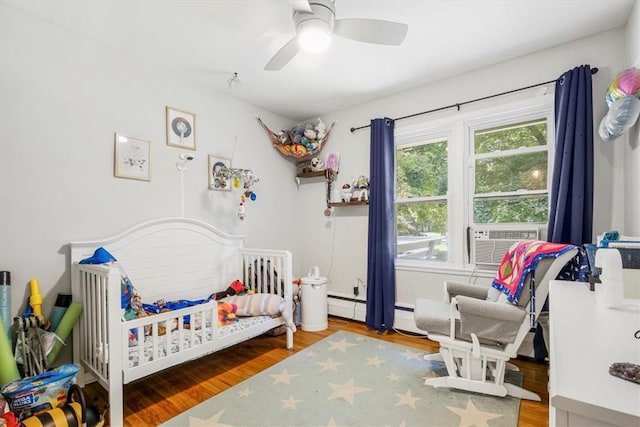 bedroom with hardwood / wood-style floors, cooling unit, ceiling fan, a baseboard radiator, and a crib