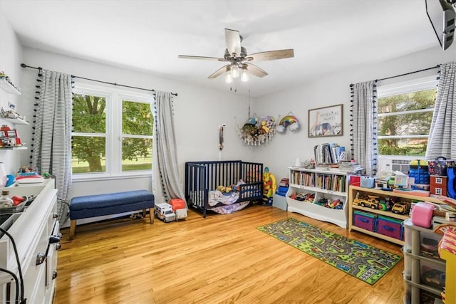 bedroom featuring a crib, light wood-type flooring, multiple windows, and ceiling fan