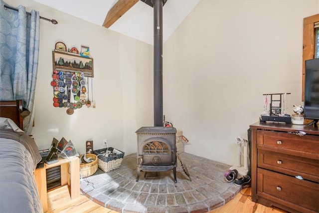 bedroom featuring vaulted ceiling, light hardwood / wood-style flooring, a wood stove, and ceiling fan