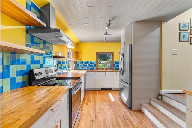 kitchen with appliances with stainless steel finishes, wall chimney exhaust hood, light hardwood / wood-style flooring, white cabinetry, and butcher block counters