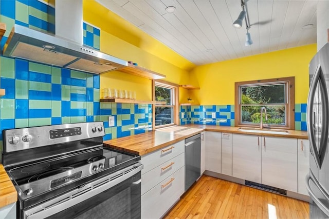 kitchen with sink, wall chimney exhaust hood, wooden counters, white cabinets, and appliances with stainless steel finishes