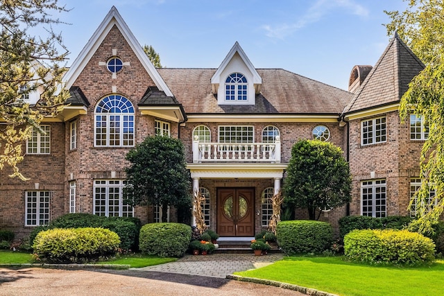 view of front of house with a balcony, a front lawn, and brick siding