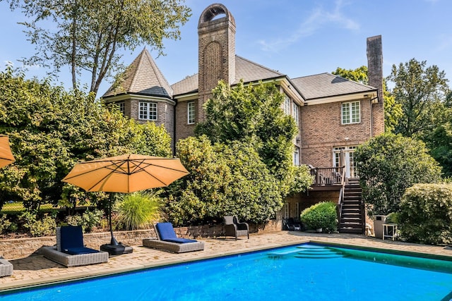 rear view of house featuring a deck, stairs, an outdoor pool, a chimney, and a patio area