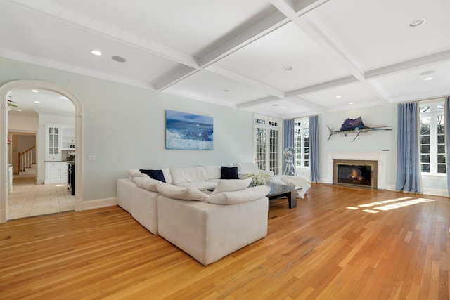 living room with arched walkways, beam ceiling, coffered ceiling, and light wood finished floors