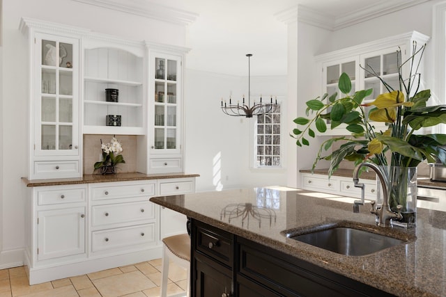 kitchen featuring a sink, white cabinetry, dark stone countertops, glass insert cabinets, and crown molding