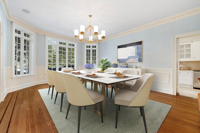 dining space featuring an inviting chandelier, crown molding, wood finished floors, and wainscoting