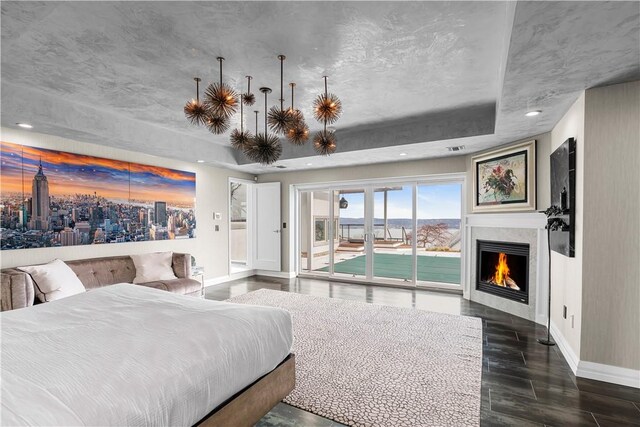 bedroom with access to exterior, dark hardwood / wood-style flooring, and a tray ceiling