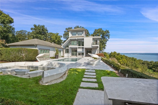 back of property with a lawn, a balcony, a water view, and a patio