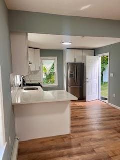 kitchen featuring white cabinets, sink, stainless steel fridge, light hardwood / wood-style floors, and kitchen peninsula