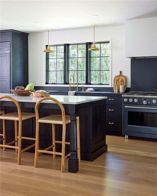 kitchen featuring stainless steel range, a center island, hanging light fixtures, a kitchen breakfast bar, and light wood-type flooring