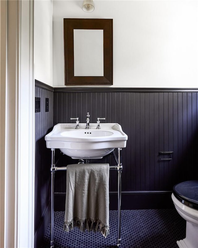 bathroom featuring tile patterned floors, toilet, wood walls, and sink