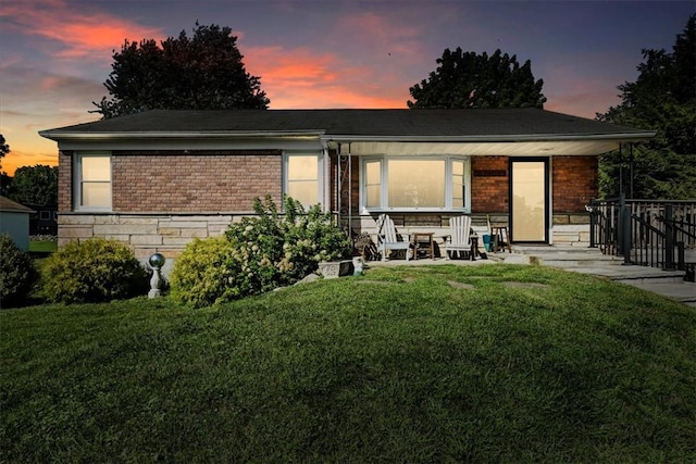 back house at dusk with covered porch and a yard