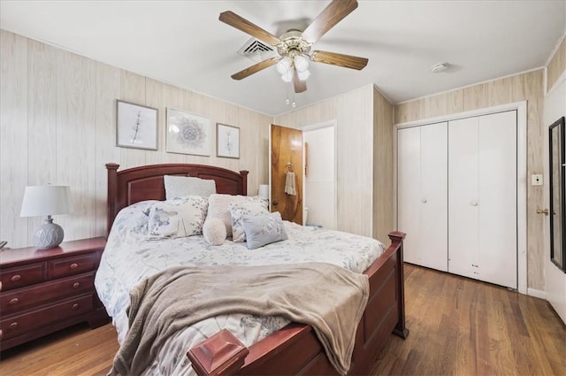 bedroom with hardwood / wood-style floors, ceiling fan, wood walls, and a closet