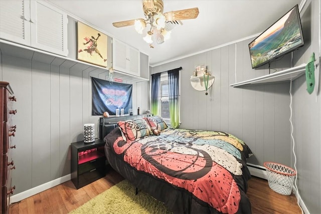 bedroom with ceiling fan, a baseboard radiator, wood walls, hardwood / wood-style floors, and ornamental molding