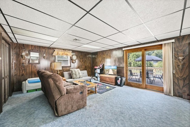 carpeted living room with a drop ceiling, plenty of natural light, and wooden walls