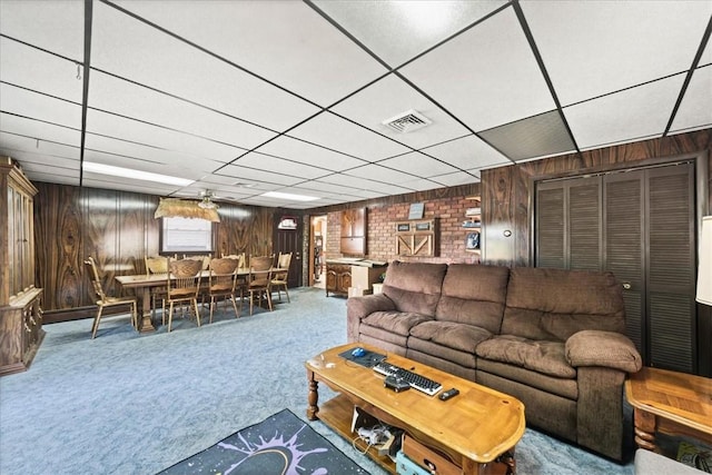 carpeted living room with a drop ceiling and wood walls