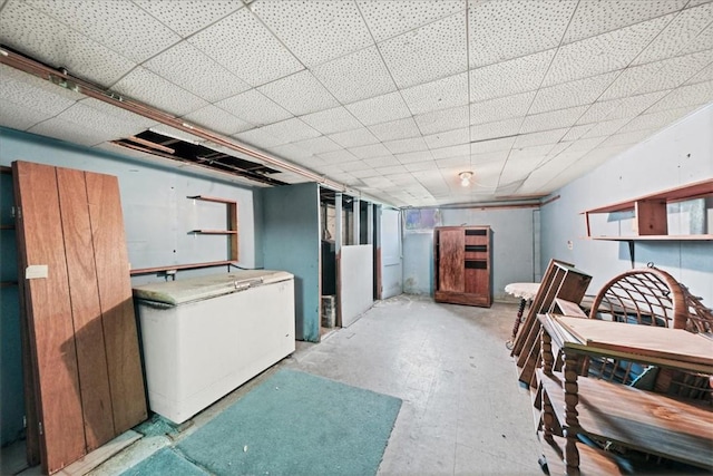 basement featuring a drop ceiling and white refrigerator