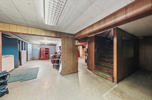 basement with a paneled ceiling and wood walls