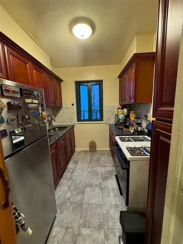 kitchen featuring tasteful backsplash, dark stone counters, white range with gas cooktop, sink, and stainless steel refrigerator