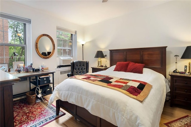 bedroom with cooling unit, light hardwood / wood-style floors, radiator, and multiple windows