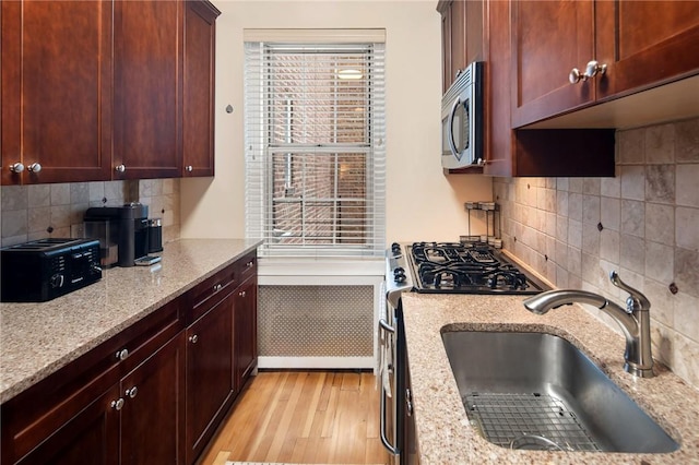 kitchen featuring backsplash, sink, light hardwood / wood-style flooring, light stone counters, and stainless steel appliances