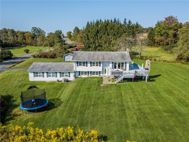 rear view of house featuring a trampoline, a yard, and a wooden deck