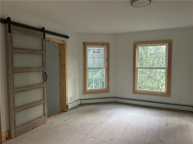 empty room featuring a barn door, light hardwood / wood-style flooring, and baseboard heating