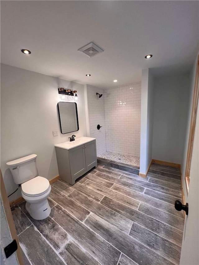 bathroom with a tile shower, vanity, and toilet