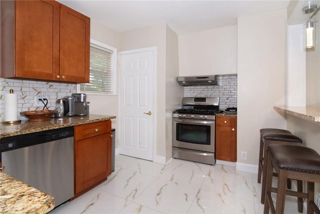 kitchen with light stone countertops, appliances with stainless steel finishes, decorative backsplash, and exhaust hood