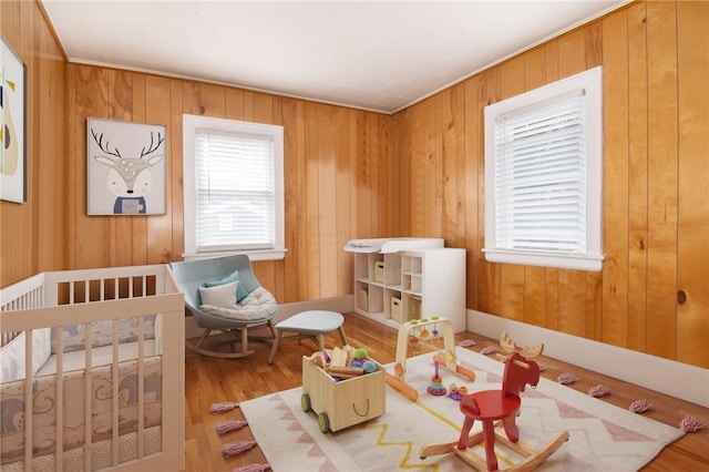 bedroom with wood-type flooring, a nursery area, and wooden walls