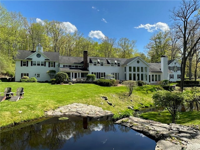 back of house with a lawn and a water view