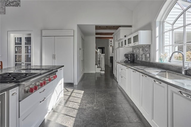 kitchen with white cabinetry, sink, stainless steel gas cooktop, tasteful backsplash, and lofted ceiling