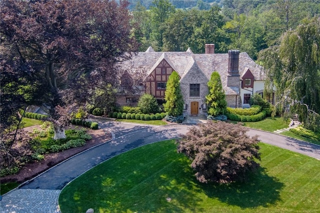 tudor home featuring a front yard, stone siding, driveway, and a chimney