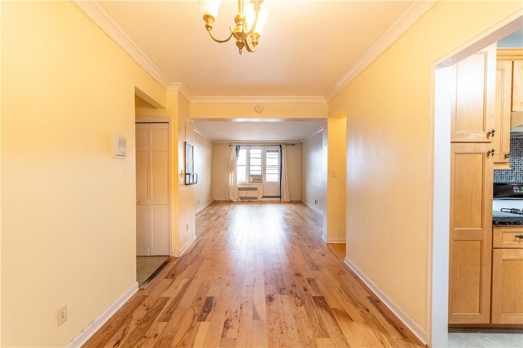 corridor featuring crown molding, light hardwood / wood-style floors, and an inviting chandelier