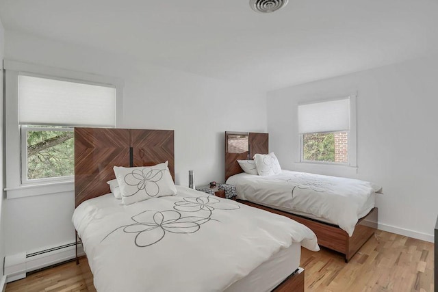 bedroom with multiple windows, a baseboard radiator, and light hardwood / wood-style flooring