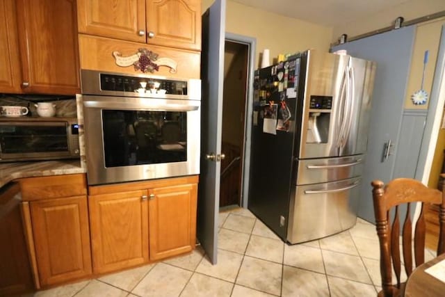 kitchen featuring decorative backsplash, a barn door, light tile patterned flooring, and appliances with stainless steel finishes