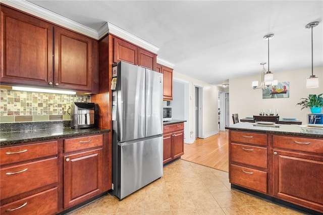 kitchen with hanging light fixtures, light hardwood / wood-style flooring, tasteful backsplash, stainless steel refrigerator, and a chandelier