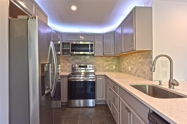 kitchen with tasteful backsplash, light stone counters, stainless steel appliances, sink, and gray cabinets