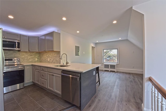 kitchen with gray cabinetry, sink, dark hardwood / wood-style flooring, kitchen peninsula, and appliances with stainless steel finishes