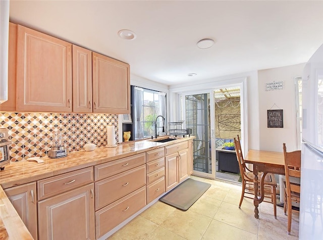 kitchen with sink, light brown cabinets, wooden counters, backsplash, and light tile patterned floors