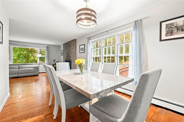 dining space featuring a notable chandelier, a fireplace, light wood-type flooring, and baseboard heating