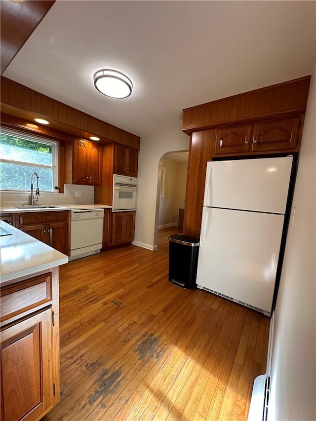 kitchen featuring a baseboard heating unit, sink, white appliances, and light wood-type flooring