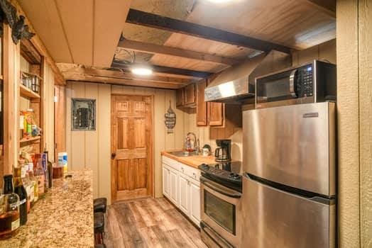 kitchen featuring sink, stainless steel appliances, light stone counters, light hardwood / wood-style flooring, and beamed ceiling