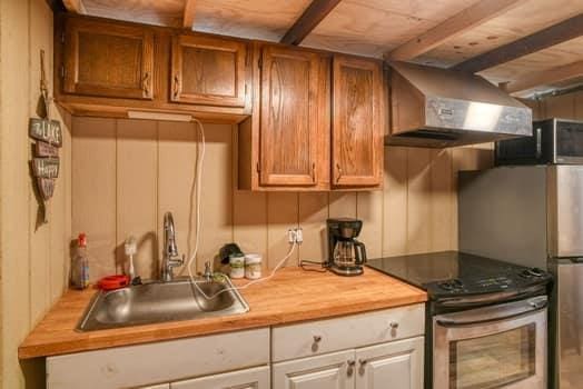 kitchen featuring stainless steel range with electric cooktop, wooden counters, ventilation hood, white cabinets, and sink