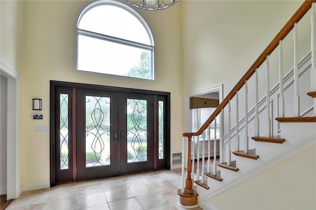 entrance foyer featuring french doors, a towering ceiling, light tile patterned floors, and an inviting chandelier