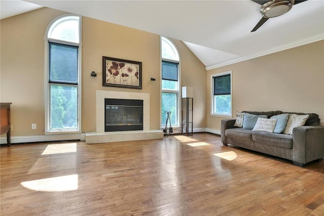 living room featuring vaulted ceiling, ceiling fan, a baseboard heating unit, light hardwood / wood-style flooring, and a tiled fireplace