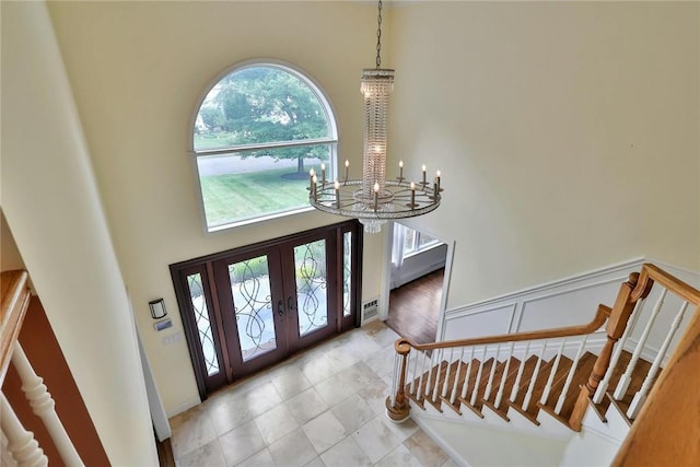 foyer featuring plenty of natural light, french doors, a towering ceiling, and an inviting chandelier