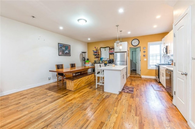 kitchen with white cabinets, decorative light fixtures, a kitchen island, a kitchen bar, and stainless steel appliances