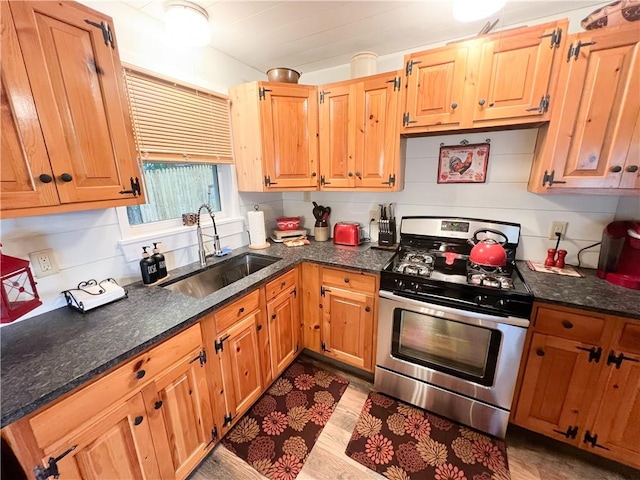 kitchen featuring gas stove, backsplash, dark stone counters, and sink