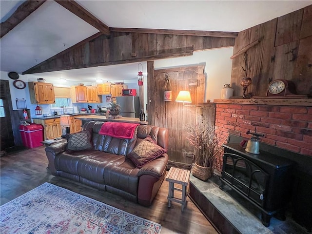 living room with wood walls, a wood stove, lofted ceiling with beams, sink, and dark hardwood / wood-style floors